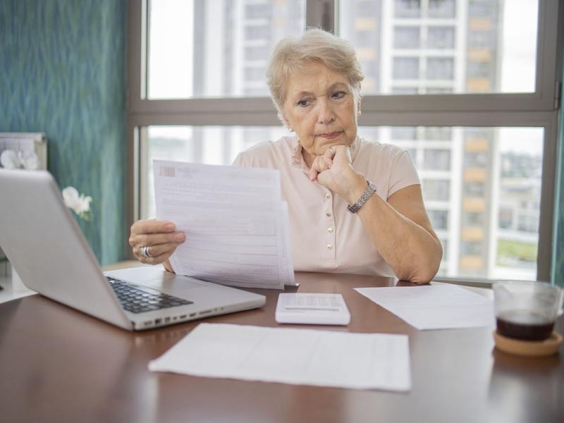 Older woman reviewing paperwork while working on a laptop