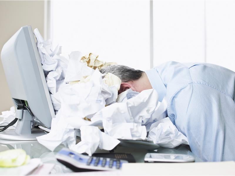 Person with their head on a desk, surrounded by crumpled paper
