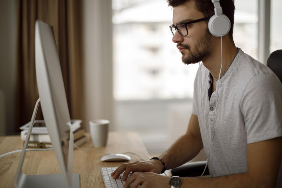 Man wearing glasses and headphones typing at a desktop computer.