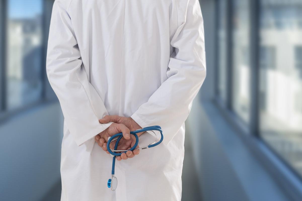 Physician holding stethoscope behind their back