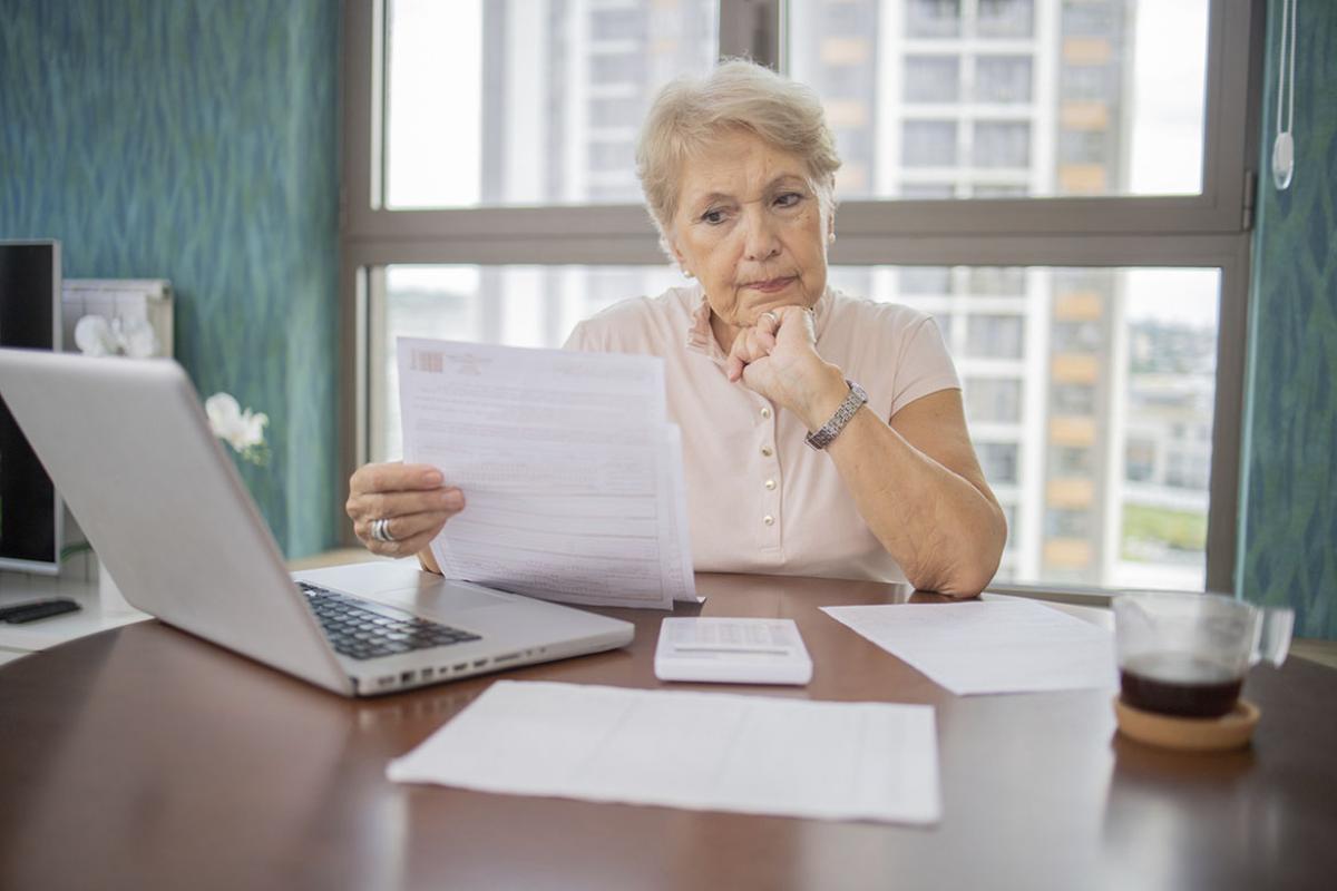 Older woman reviewing paperwork while working on a laptop