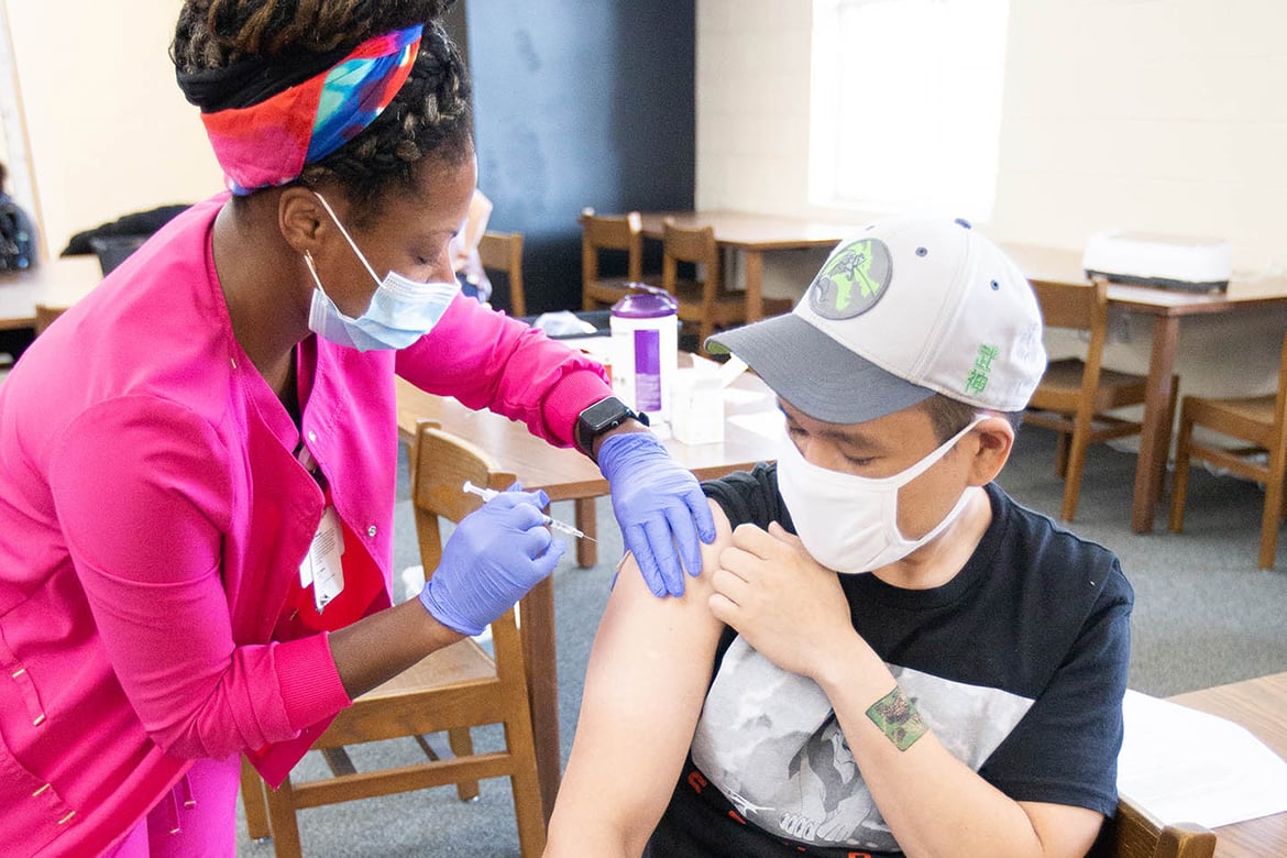Health care worker vaccinating a young teen, both wearing masks