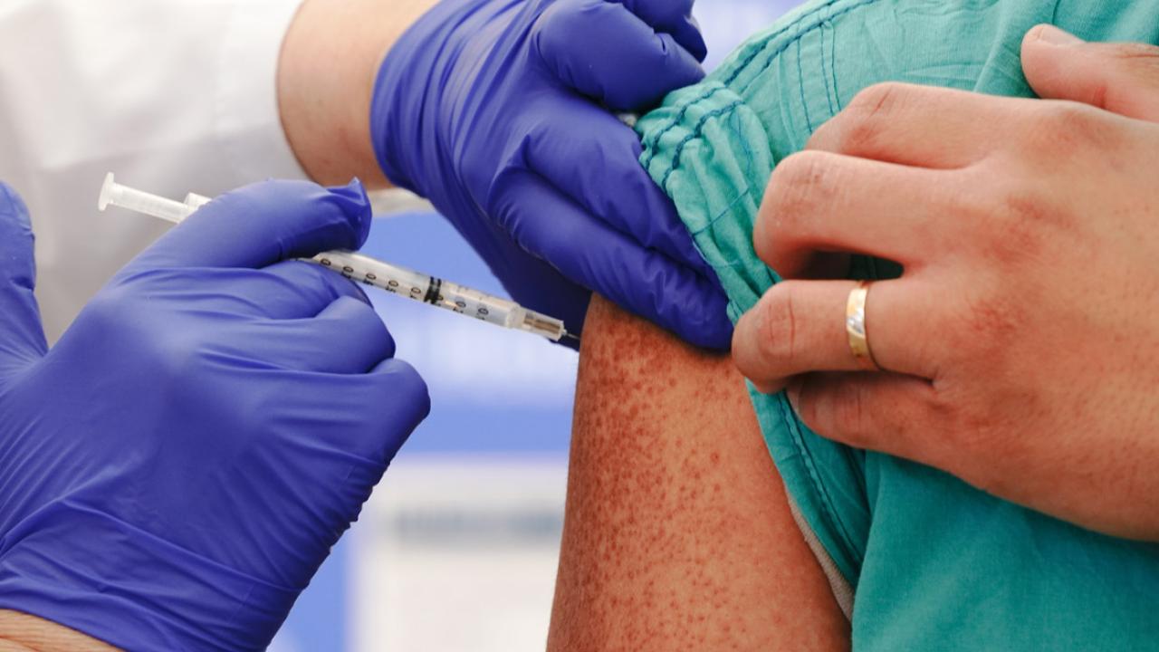 Close up of health professional wearing gloves inoculating person with a vaccine on their right arm.