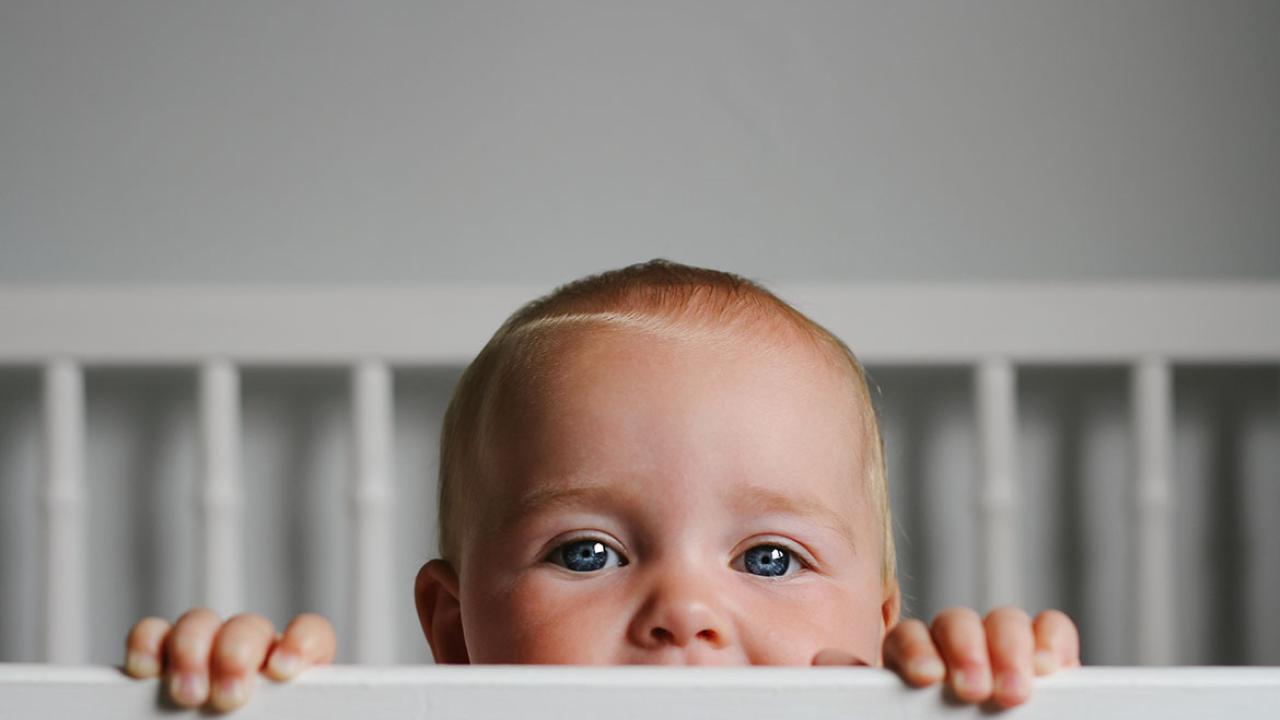 Baby peeking out over the top of a crib