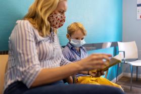 A mother and her young son, both masked, sitting in a hospital or patient waiting room