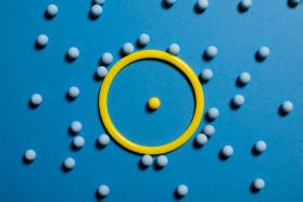 One yellow ball in yellow ring, many blue balls outside of ring on blue surface