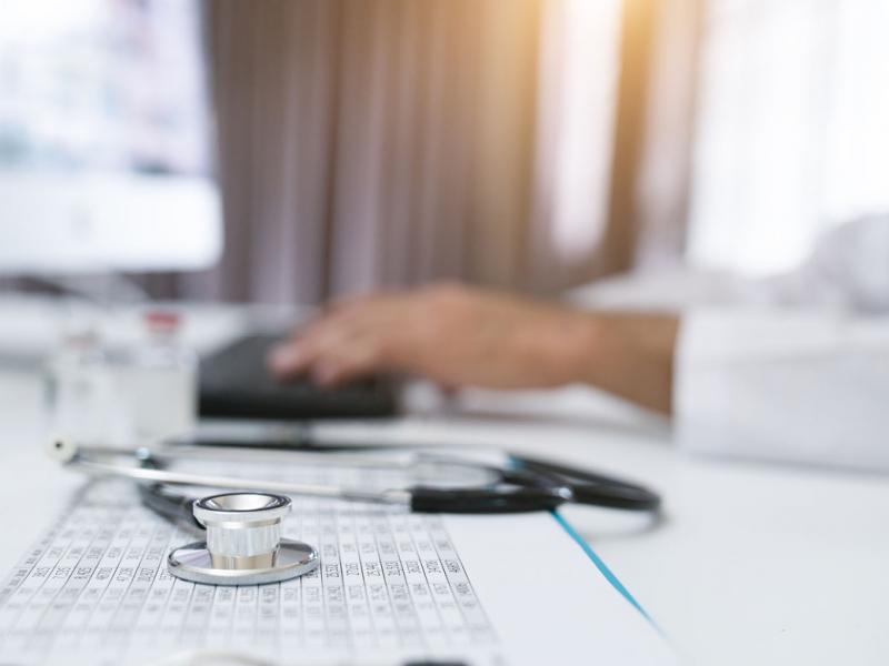 Stethoscope next to a physician working on a computer