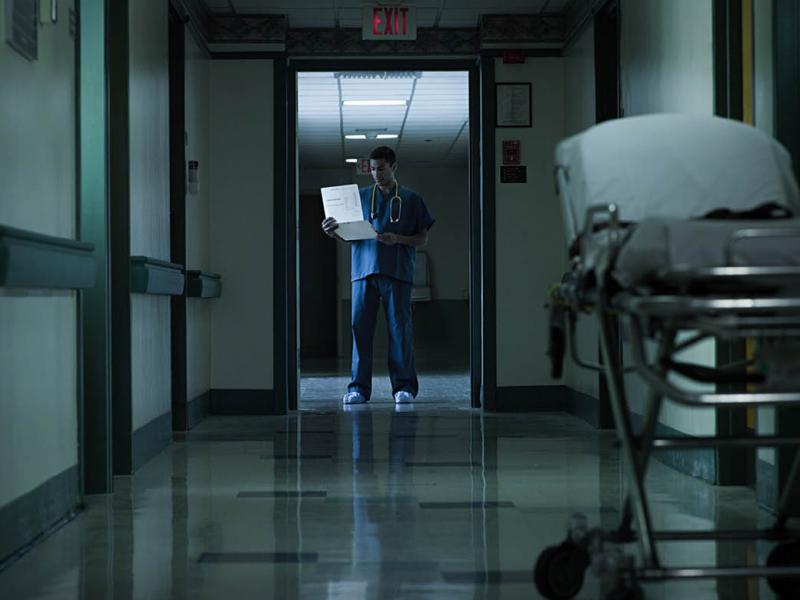 Physician standing in hospital hallway, looking at a chart