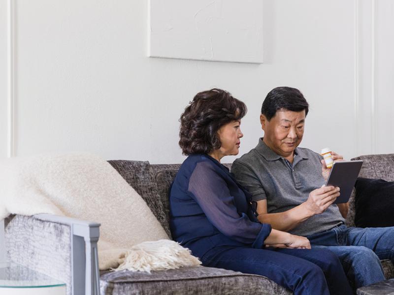 Man and woman sitting on a sofa with an iPad, medicine bottle in man's hand