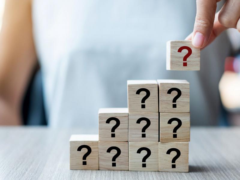 Close-up of hand stacking wooden blocks with question marks on them.