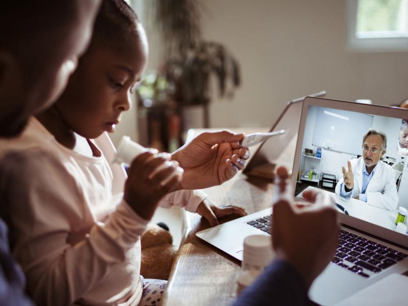 Parent and child speaking with a doctor through a telemedicine session on a laptop.