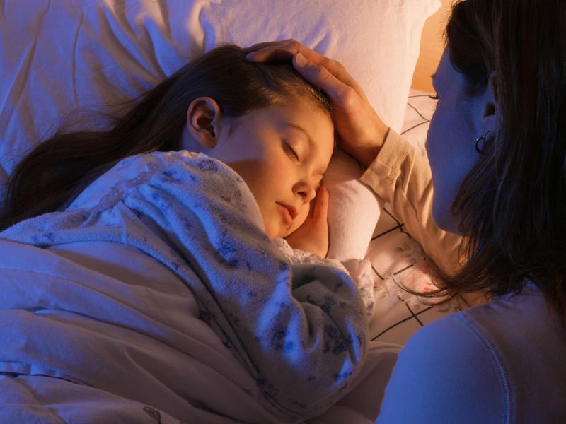 Mother tucking her daughter into bed.