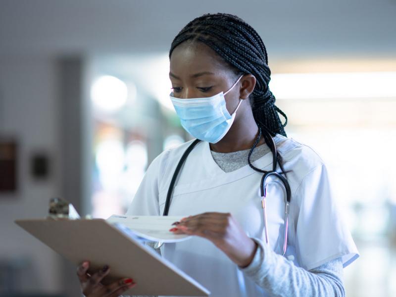 A masked doctor checking information on a clipboard.