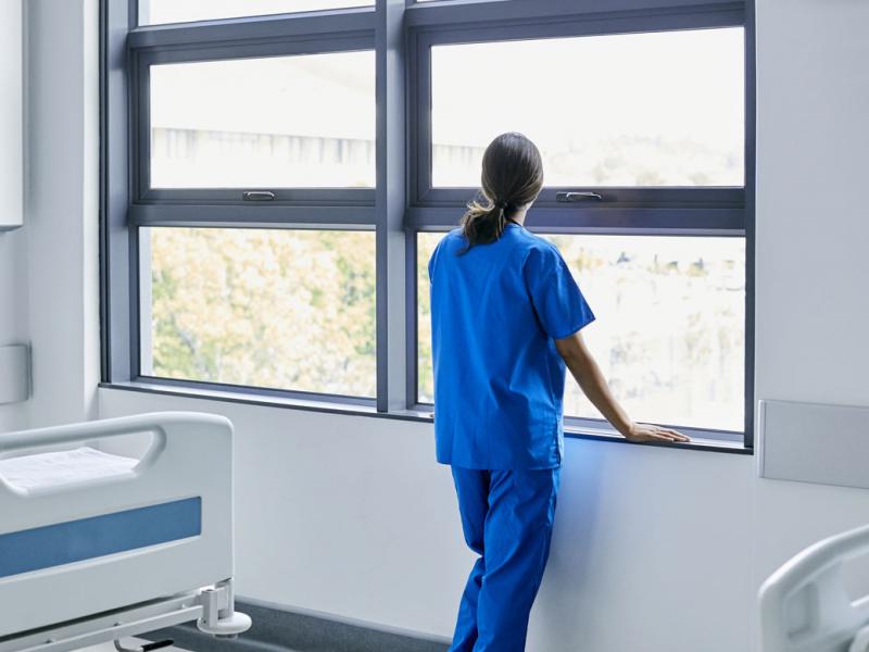 Doctor in scrubs looking out the window of an empty hospital room.