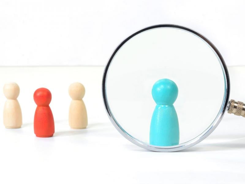 Graphic of painted wooden figures, with magnify glass