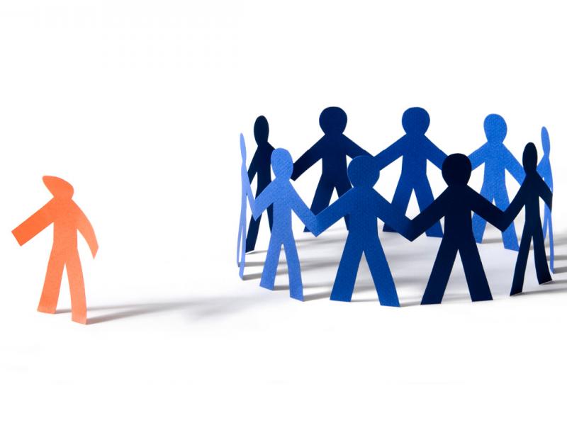  Orange paper person with dejected stance off to the side of a circle of blue paper people