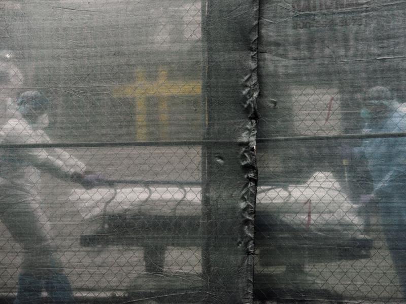 Medical workers wheel a deceased patient on a stretcher behind a privacy screen 