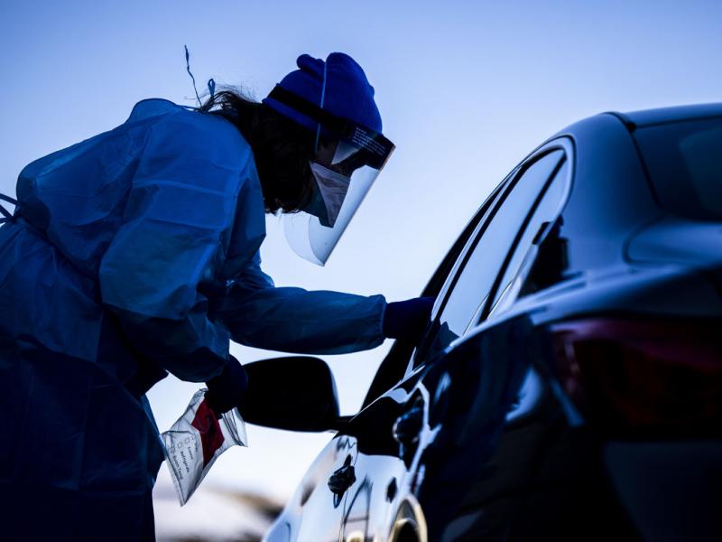 Health care professional in PPE standing outside of a car