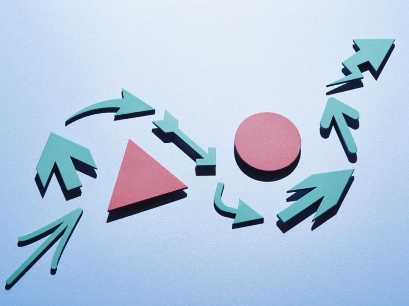 A series of light blue arrows of different shapes and design making an s-curve around a pink triangle and pink circle.