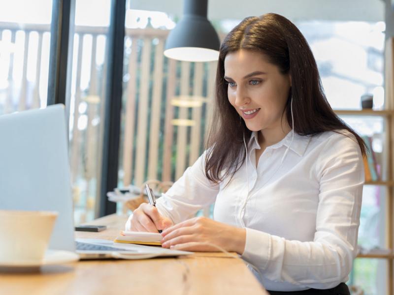 A woman with dark hair working at a laptop while wearing ear buds.