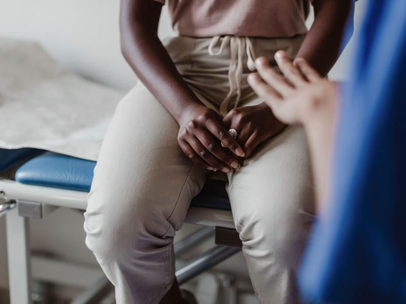 An African-American patient sitting on an examination table in the background with a health care working in the far right of the foreground.