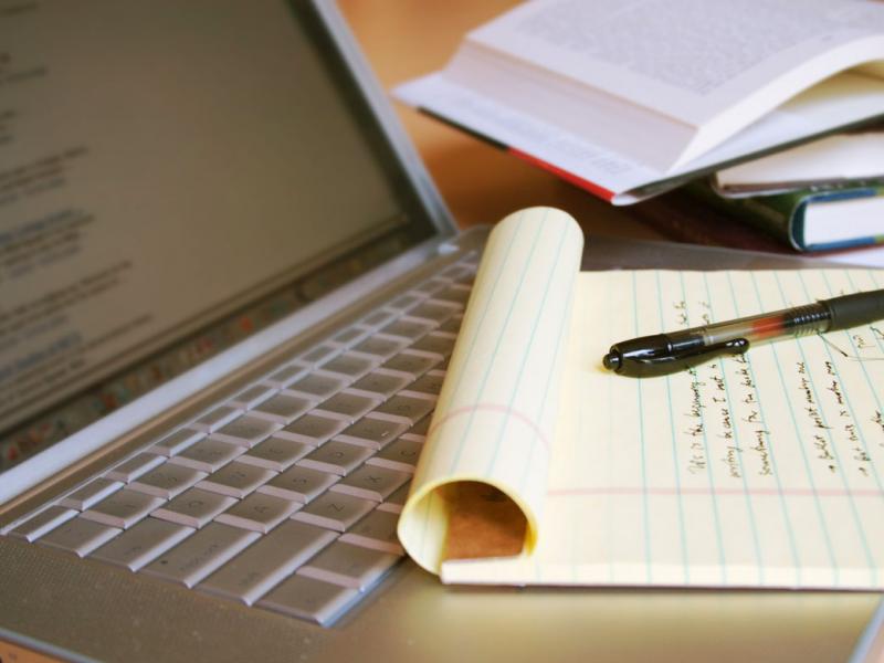 Photo of an open laptop with text on the screen with a yellow legal pad on top of the keys.