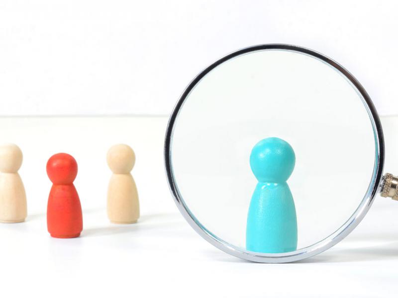 Different colors of figurines with one under a magnifying glass