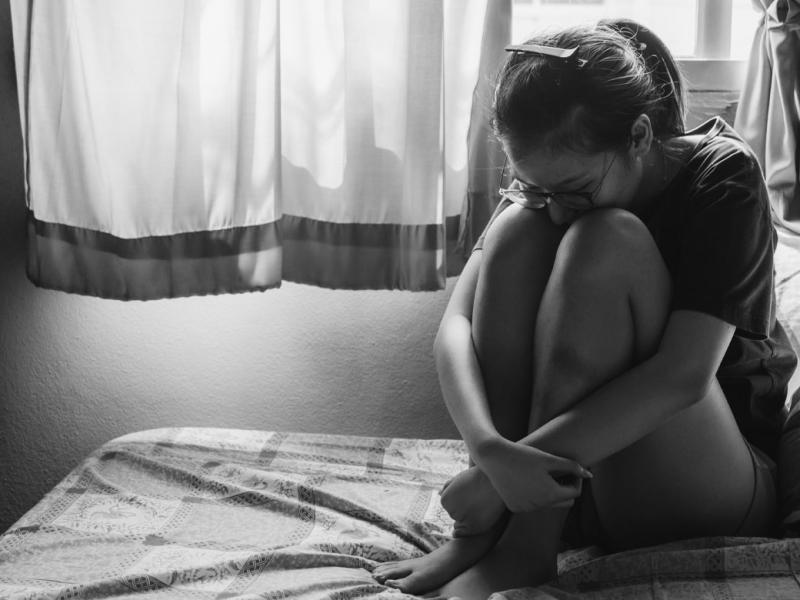 Person sitting alone in a dark bedroom
