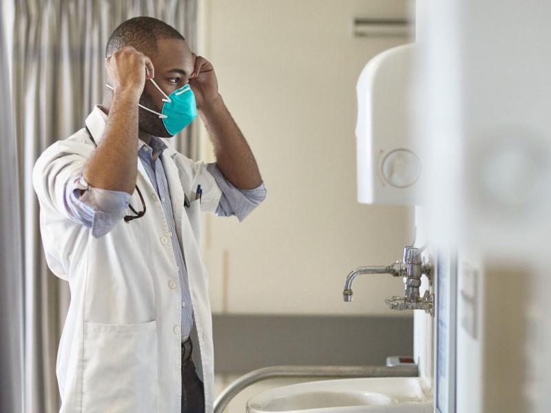 Physician adjusting a mask in front of a mirror and sink