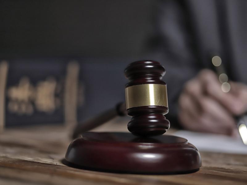 Close-up of a judge's gavel with a blurred out judge writing in the background.