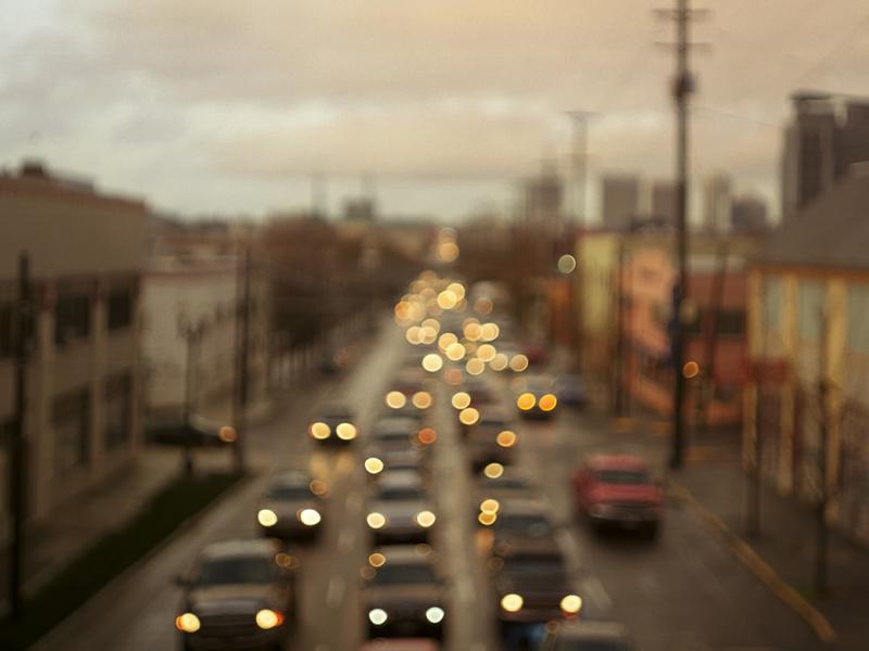 A blurred shot of a town street crowded with automobile traffic at dusk.