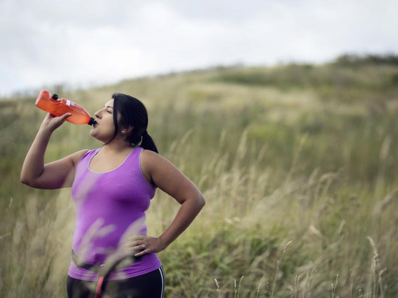 Woman pausing in a field during a hike or walk to take a drink from a bottle of water or an energy drink.