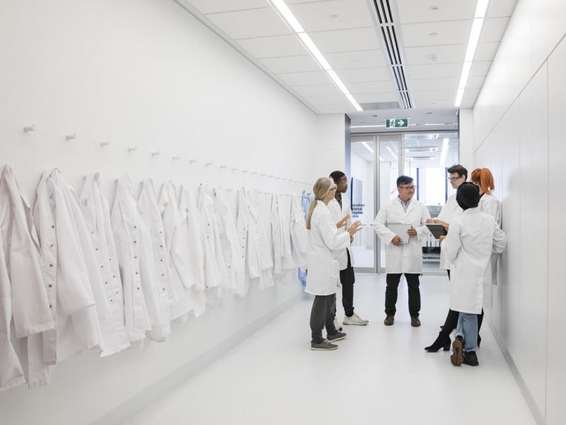 Group of physicians standing in a corridor with white physician coats hanging on racks on a left side wall.