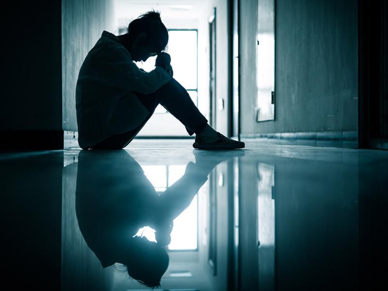 Young woman sitting on the floor in a hallway with her head on top of her knees.