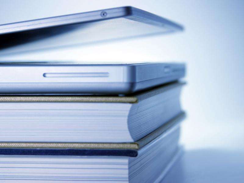 Slightly open laptop lying on top of stack of books