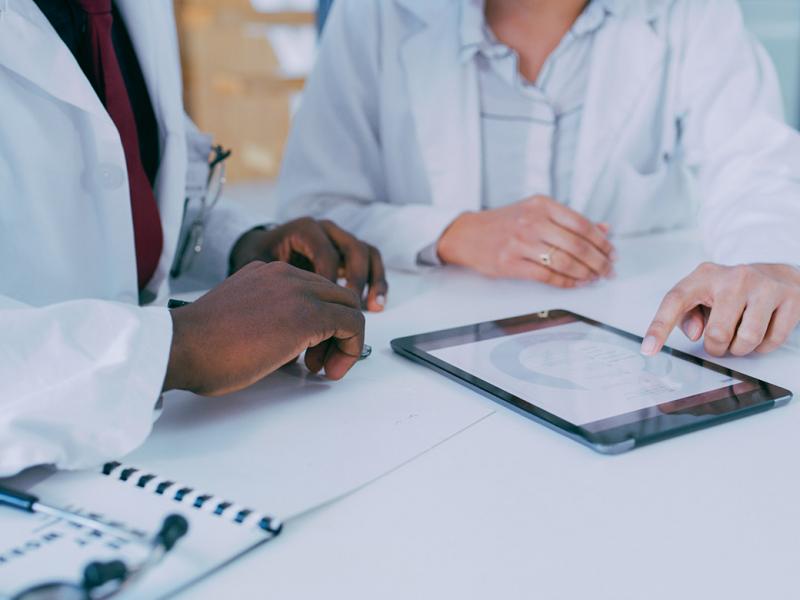 Close up of two physicians reviewing patient medical information or medical research on a pad.