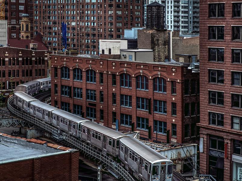 An elevated/subway train rounding a curve next to some city buildings
