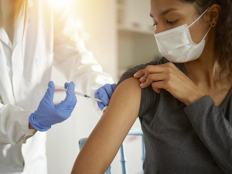 Woman wearing a mask and rolling up her sleeve to get a vaccination from a physician