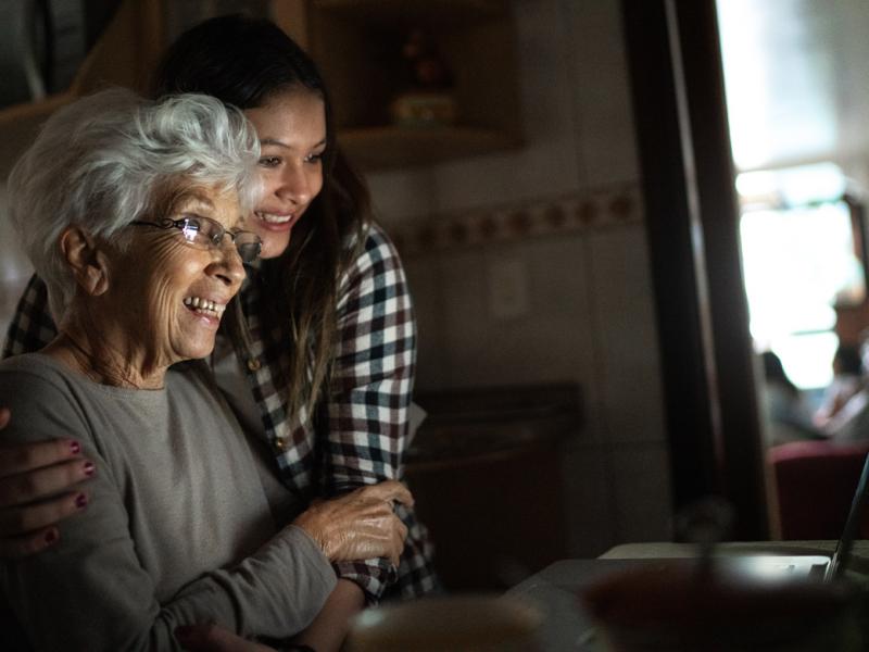 A grandmother and granddaughter viewing a laptop screen and embracing