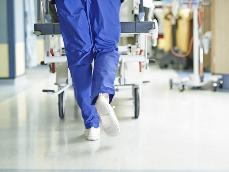 Tight shot of health care worker in scrubs pushing a gurney down a hospital hallway