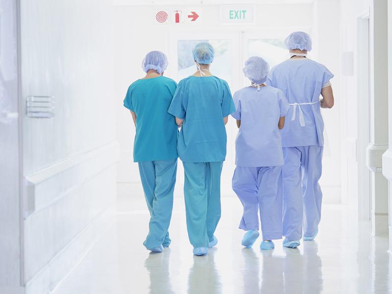 View from the back of four health care professionals wearing scrubs exiting an operating room