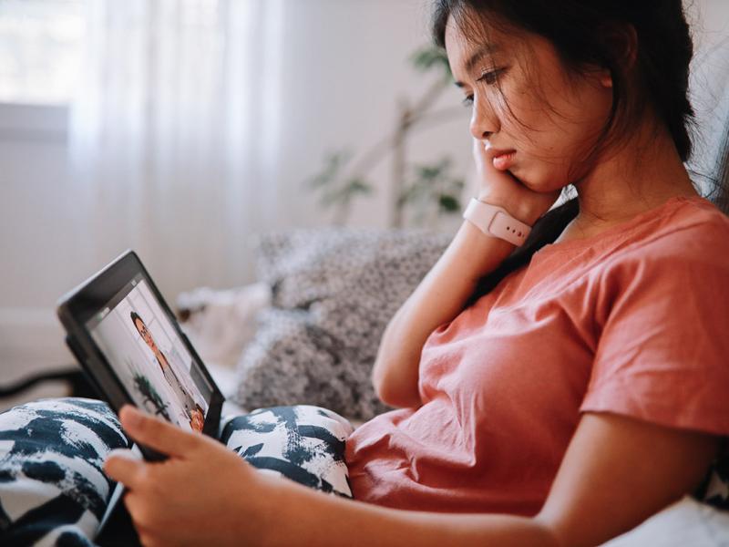 Woman sitting on a sofa with a computer tablet having a telehealth conference with a physician
