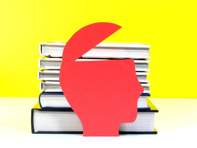 A paper cut out of a human head with a stack of books behind it