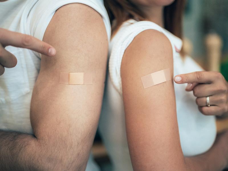 Two people pointing at their arms where they received a vaccine