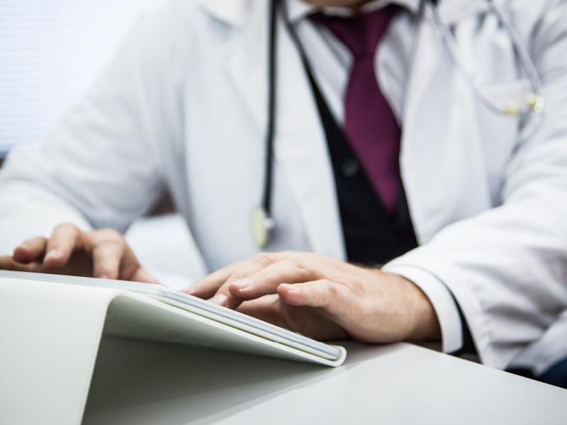 Close up of physician typing on tablet positioned on a stand or holder