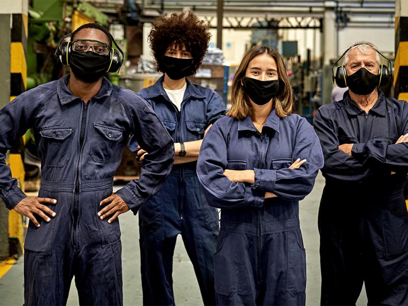 Group of metal workers in coveralls, protective eyewear, ear protectors, and face masks 