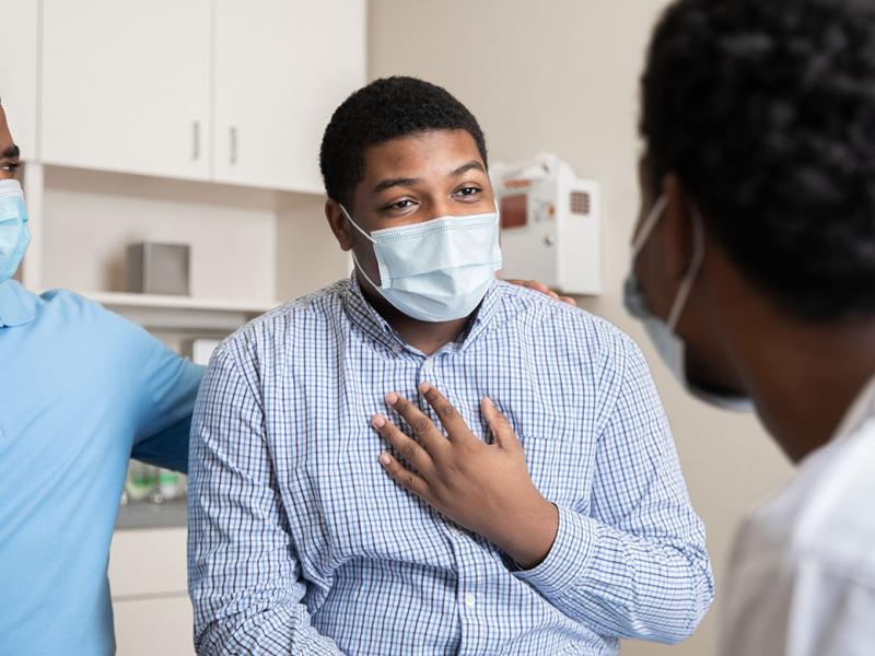 Masked patient holding hand to chest and speaking with physician