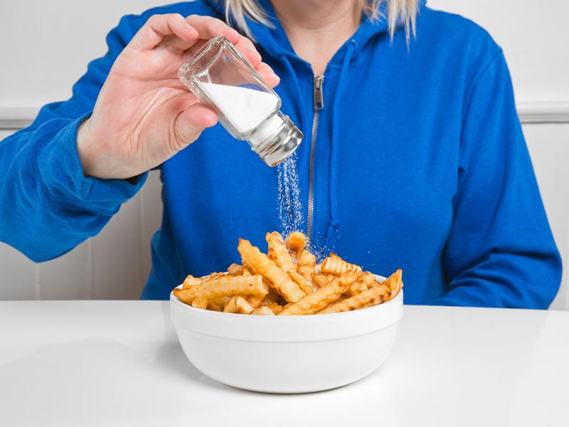 Person salting a bowl of french fries