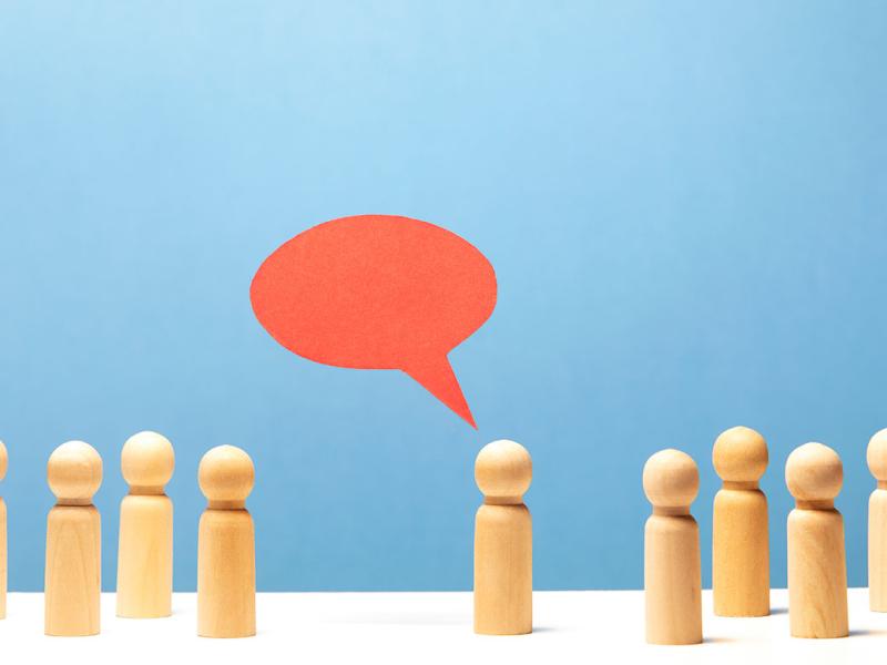 Red speech bubble in mid air over wooden figurine surrounded by 8 other figurines