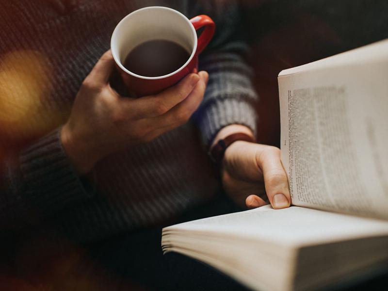 Person reading a book and drinking a hot drink from a mug